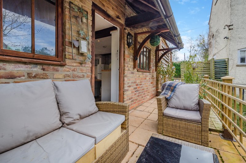 Brick cottage patio with wicker seating, cushions, wooden pergola and garden fence