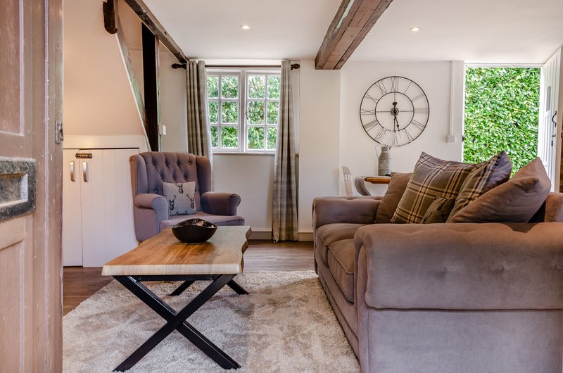 Spacious living room with brown sofa, armchair, wooden coffee table, large wall clock and windows