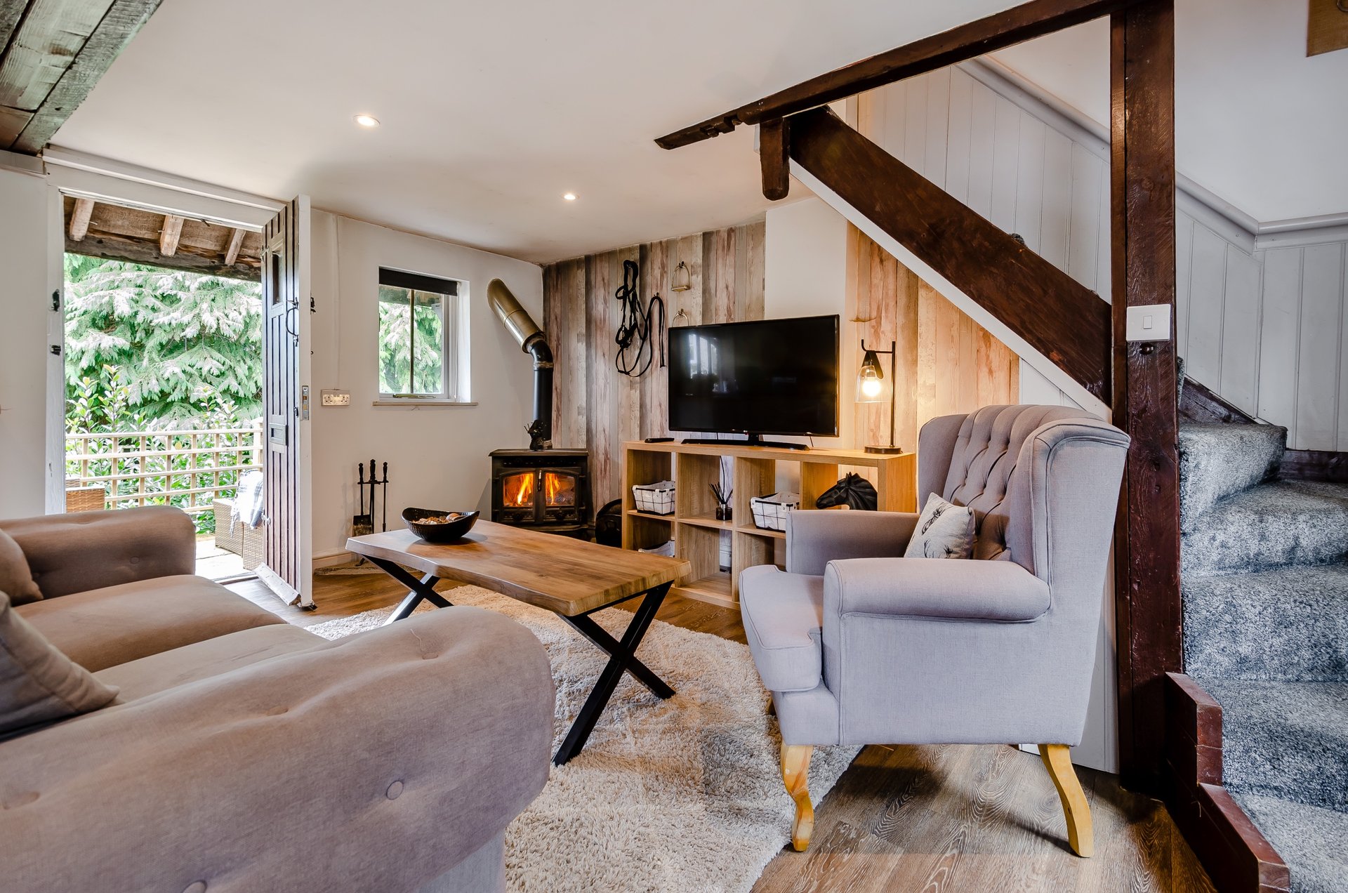 Open-plan living room with brown sofa, grey armchair, wooden TV unit, staircase and patio doors