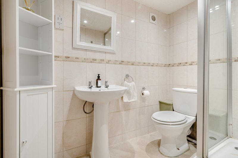 Clean bathroom with pedestal sink, toilet, shower enclosure and mirrored cabinet