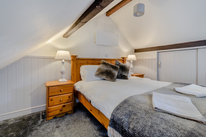 Bright attic bedroom with wooden bed, bedside tables, white walls and exposed beams