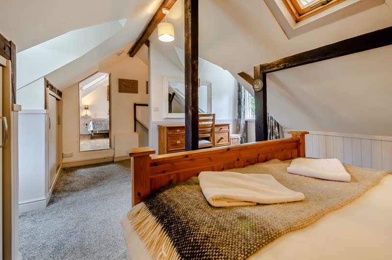 Spacious bedroom with wooden four-poster bed, cream bedding, exposed beams and vaulted ceiling