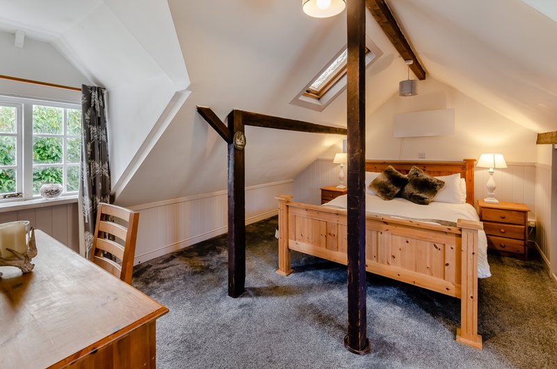 Attic bedroom with wooden four-poster bed, desk, window, and exposed beams