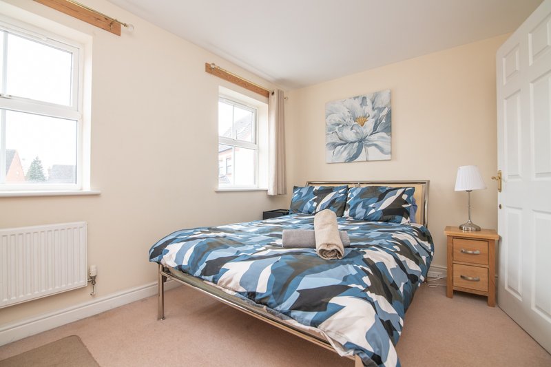 Bright bedroom with double bed, blue patterned bedding, wooden nightstand and windows