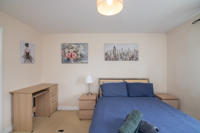 Bedroom with double bed, blue bedding, wooden desk, and framed wall art