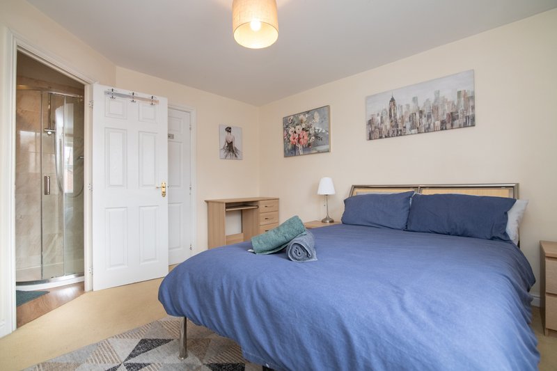 Bright bedroom with double bed, blue bedding, wooden furniture and ensuite bathroom visible