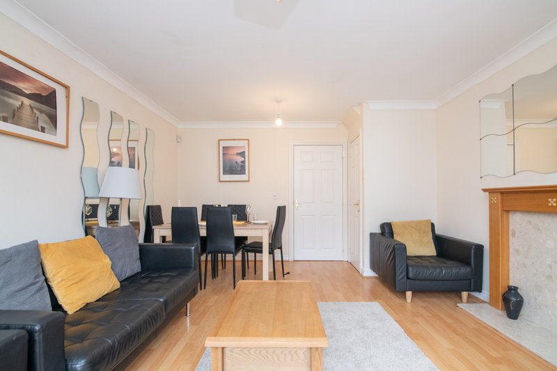 Open-plan living and dining room with black leather sofas, wooden dining table and chairs, hardwood flooring