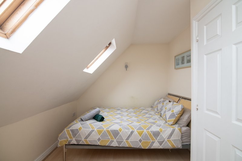 Bright attic bedroom with double bed, geometric bedding, skylight windows and white door