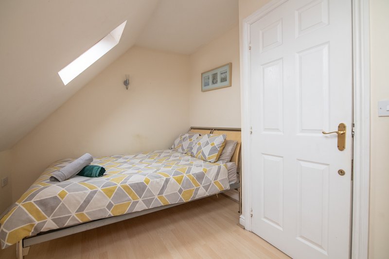 Bright attic bedroom with single bed, geometric bedding, wooden floor and white door