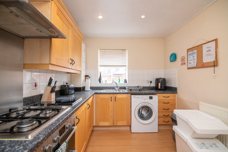 Kitchen with wooden cabinets, gas hob, washing machine, and white tile splashback