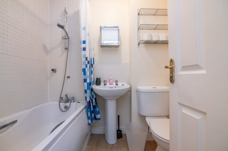 Clean bathroom with bathtub, pedestal sink, toilet, and shelving