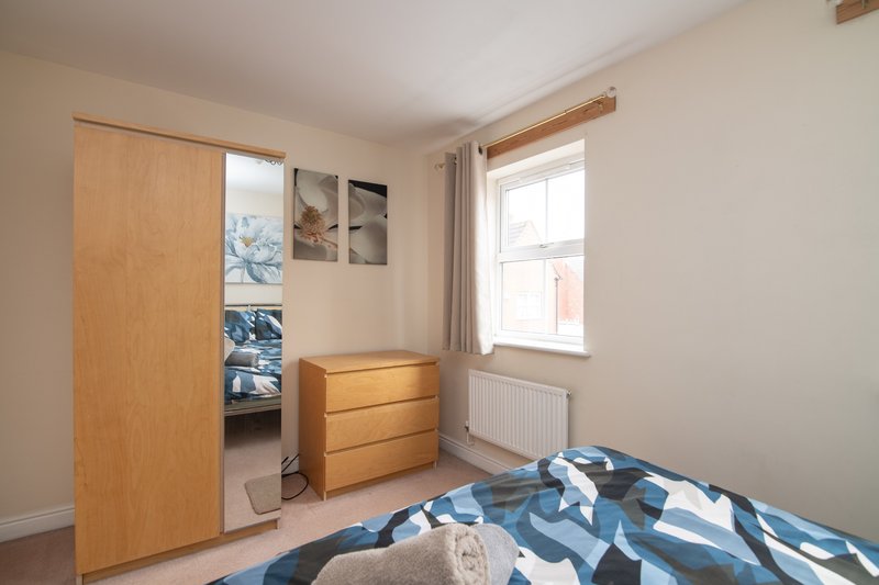 Bright bedroom with double bed, wooden wardrobe, chest of drawers, and window with natural light