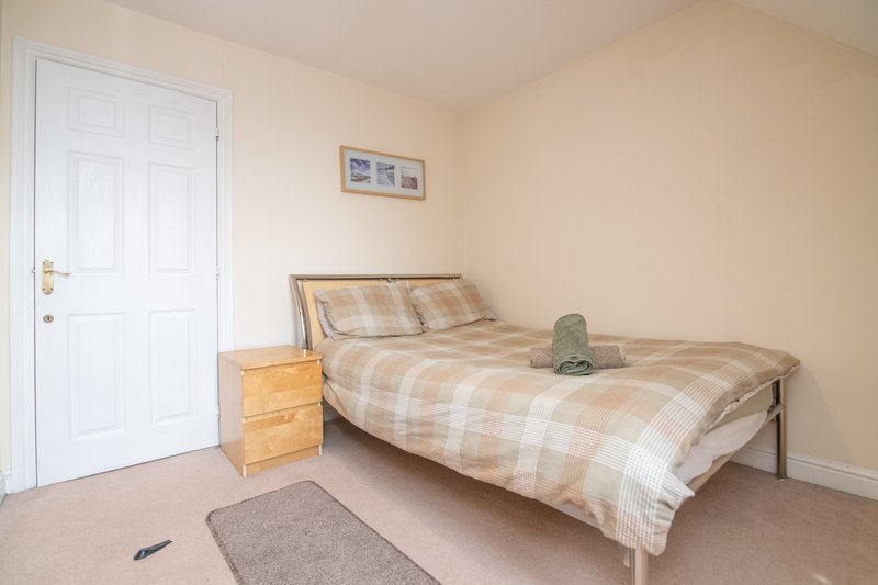 Bedroom with single bed, wooden bedside table, white door and beige walls