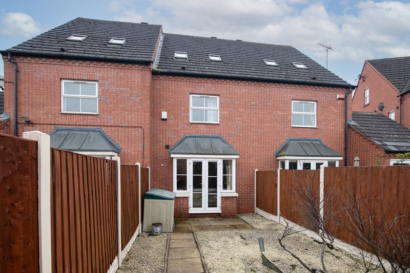 Red brick terraced house with dark roof, white-framed patio doors and driveway