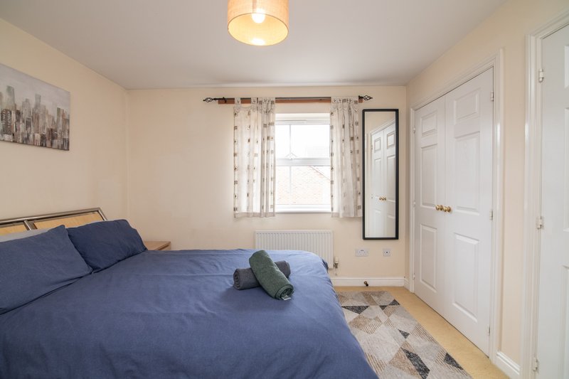 Bedroom with double bed, blue bedding, window with curtains, wooden floor and ceiling light