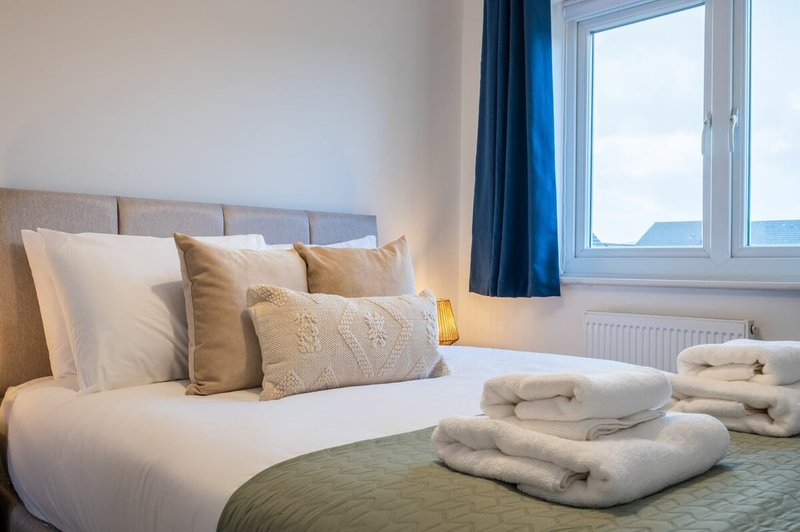 Bright bedroom with double bed, decorative pillows, folded towels and sea view from window