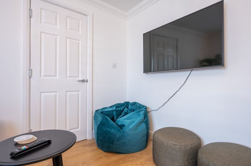 Living room with wall-mounted TV, blue bean bag chair, grey poufs, and small black table