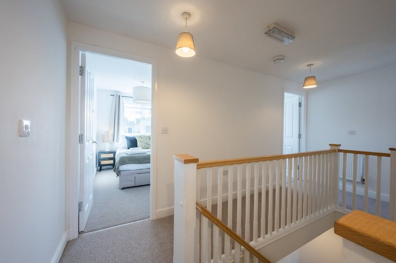 Bright hallway with staircase railing, pendant lights, and open doorway to bedroom
