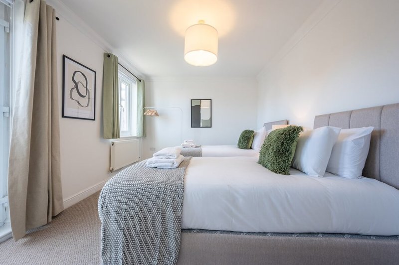 Bright bedroom with twin beds, grey headboard, white bedding and decorative cushions