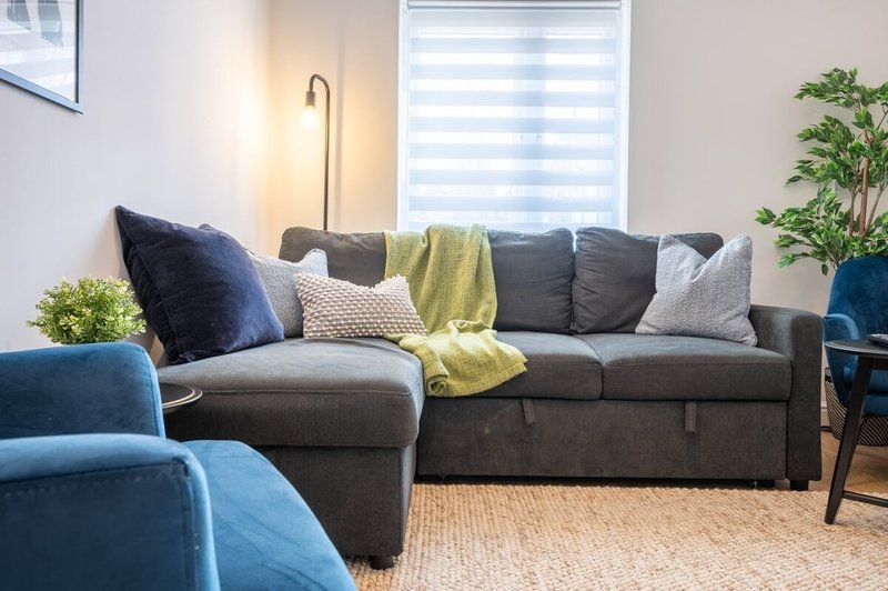 Modern living room with gray sectional sofa, blue armchair, cushions, throw blanket, potted plant and floor lamp
