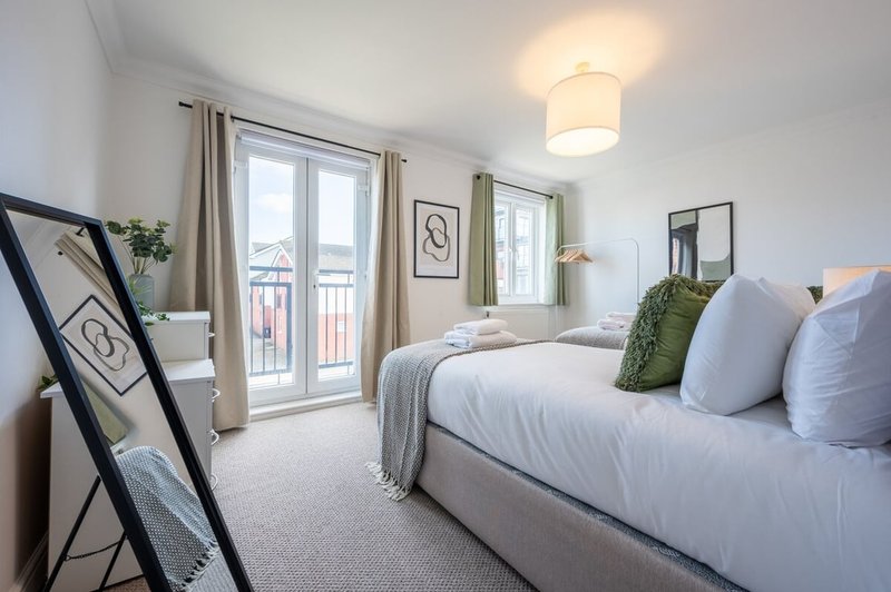 Bright bedroom with double bed, white bedding, green cushions, framed wall art, and balcony doors