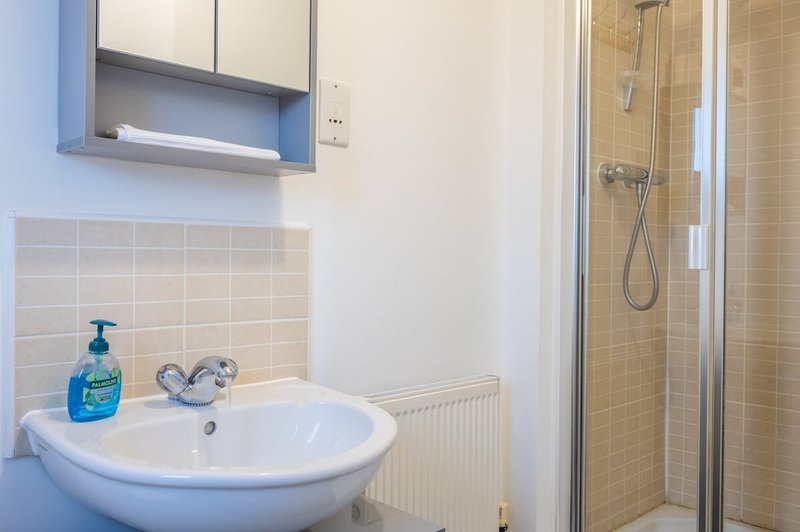 Modern bathroom with round white sink, blue soap dispenser, mirror cabinet and enclosed shower cubicle