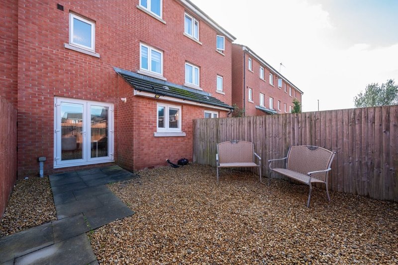 Red brick terraced house with patio area, two chairs, and wooden fence