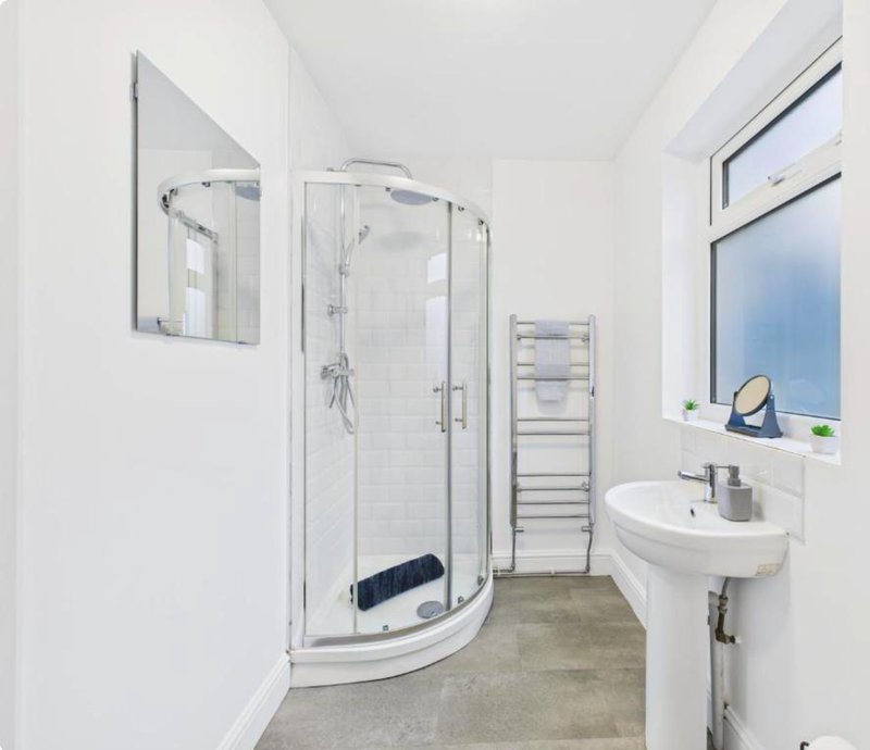 Modern bathroom with curved glass shower enclosure, wall-mounted sink, heated towel rail and mirror