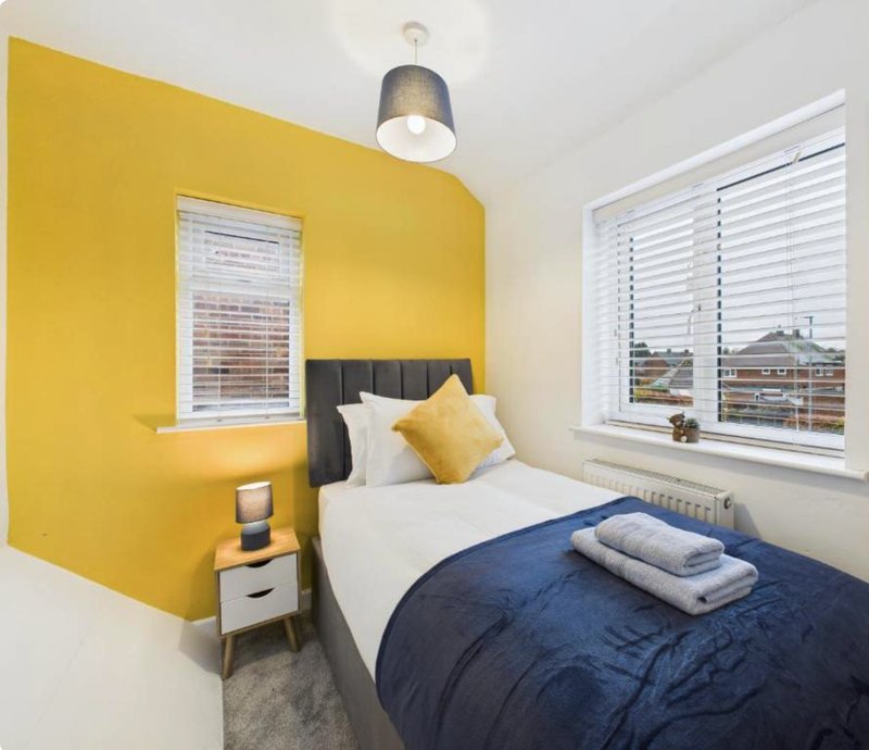 Bright bedroom with yellow accent wall, single bed, navy duvet and white pillows