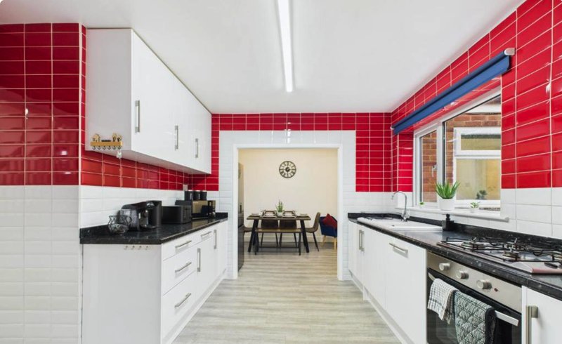 Modern kitchen with red and white tiles, white cabinetry, black countertops, and view to dining area