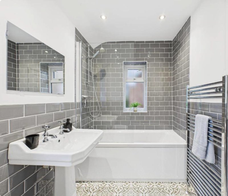Modern bathroom with gray subway tile, white pedestal sink, bathtub, and heated towel rack