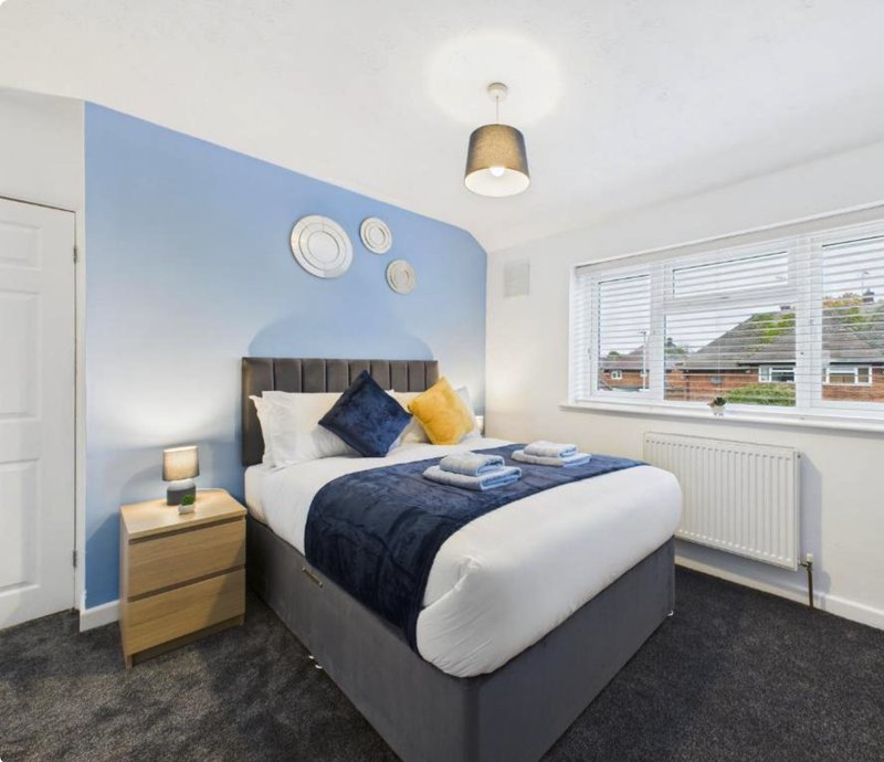 Modern bedroom with double bed, blue accent wall, wooden nightstand and large window