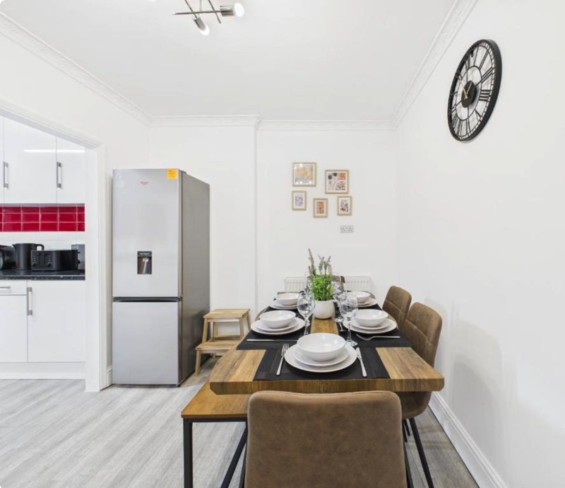 Modern kitchen-dining area with set table, stainless steel fridge, white cabinetry and wall clock