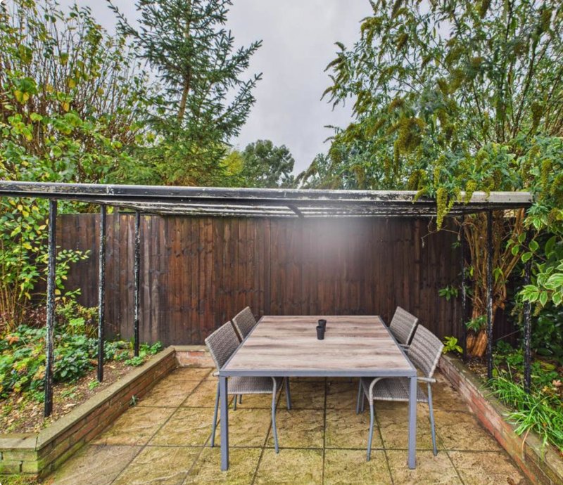 Garden patio with dining table, chairs, and pergola surrounded by green climbing plants