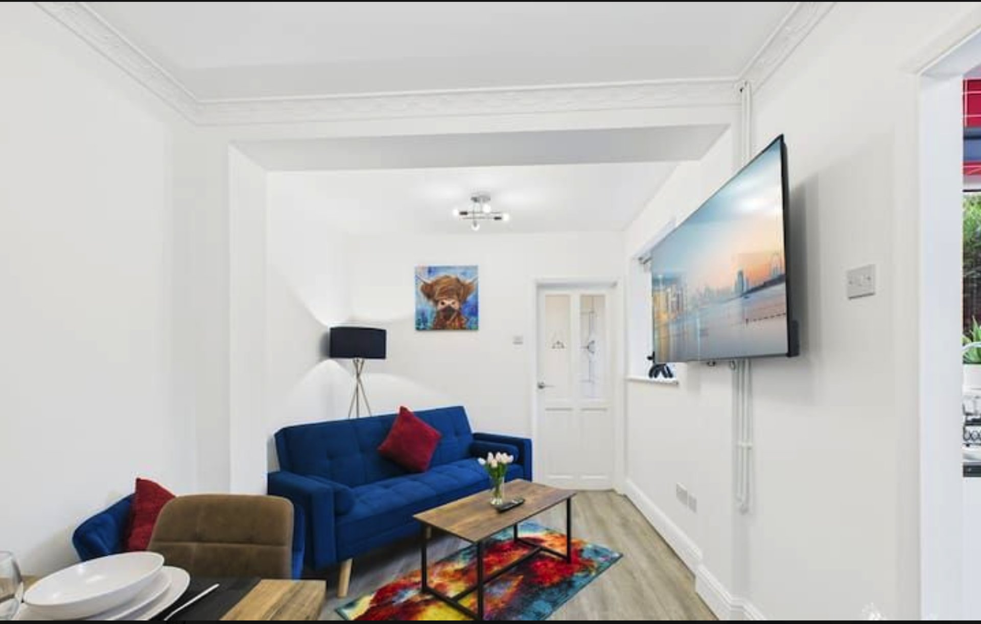 Bright living room with blue sofa, olive armchair, wooden coffee table and wall-mounted TV