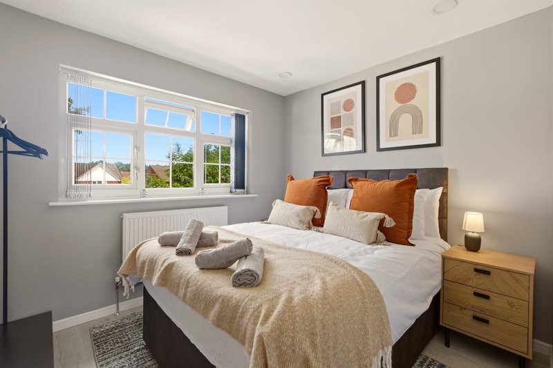Bright bedroom with double bed, wooden nightstand, orange cushions and framed wall art