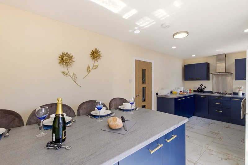 Modern kitchen with blue cabinetry, island counter, champagne bottle, and dining chairs