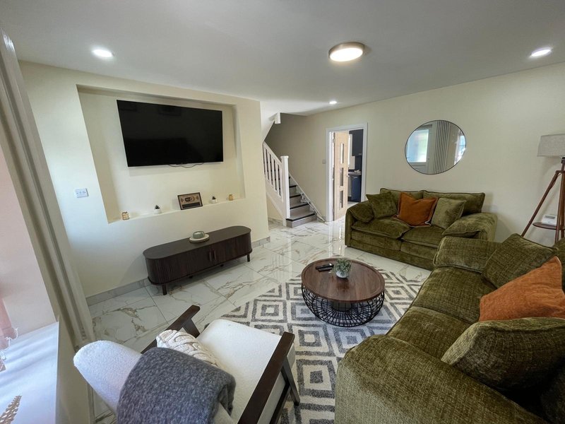 Open-plan living room with green sofa, TV wall, round coffee table and geometric rug