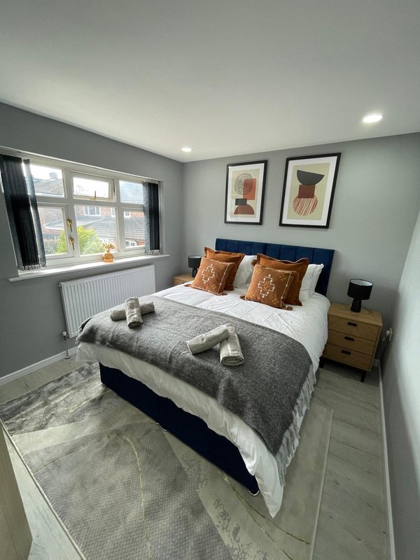 Modern bedroom with double bed, gray bedding, orange cushions, wooden nightstand and framed wall art