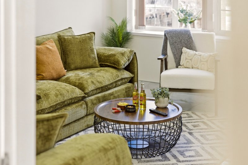 Bright living room with green upholstered sofa, round coffee table, cream armchair, and potted plants