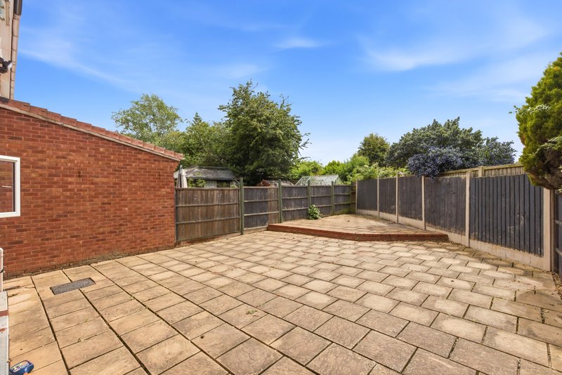 Paved garden patio with fencing, brick house wall, and surrounding mature trees