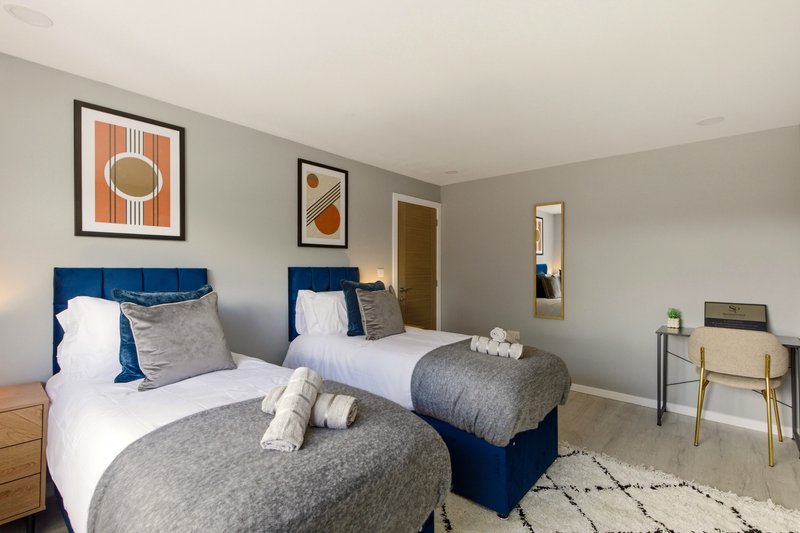 Twin bedroom with blue headboards, white pillows, gray bedding, framed wall art, and wooden furniture