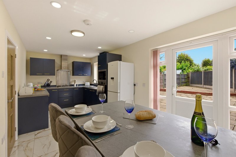 Modern kitchen and dining area with island counter, dark cabinetry, and garden view through glass doors