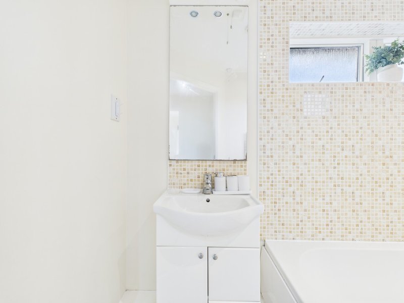 Clean bathroom with white sink vanity, mirror, small window and mosaic tile wall