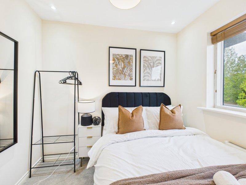 Bright modern bedroom with black headboard, white bedding, gold cushions, and framed botanical prints