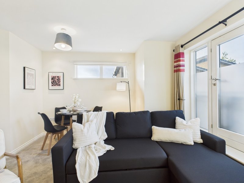 Modern living room with black corner sofa, dining table, and glass patio doors overlooking garden