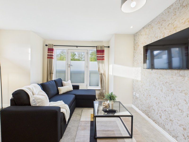 Modern living room with dark blue corner sofa, glass coffee table, wall-mounted TV and patio doors