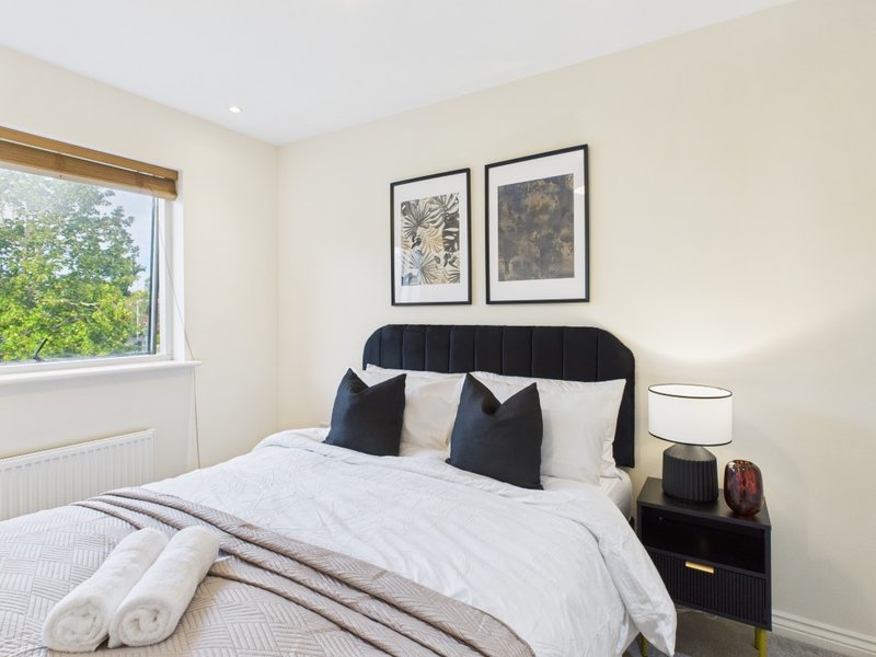 Bright bedroom with double bed, black headboard, white bedding, framed wall art, and window with garden view