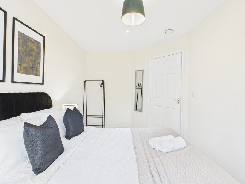 Modern bedroom with double bed, dark headboard, blue cushions, white bedding and green ceiling lamp