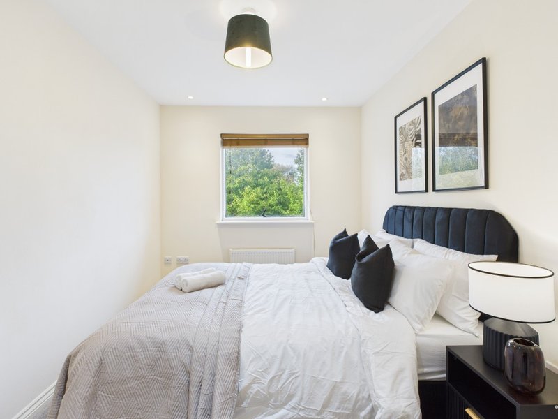 Bright modern bedroom with double bed, black headboard, framed artwork and window view